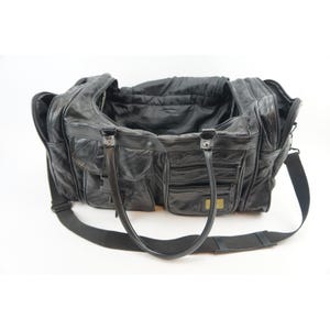May include: Black leather duffel bag with multiple pockets and compartments. Features a top handle and a detachable shoulder strap. The bag has a rectangular shape and a textured surface.