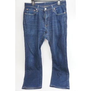 May include: Dark blue denim jeans with a classic five-pocket design. The jeans have a button and zipper closure, and a slight bootcut leg opening. The jeans are hanging on a black hanger against a white background.
