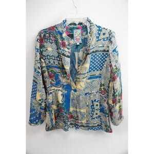 May include: A long-sleeve blazer featuring a multi-colored patchwork pattern of blue, cream, and red floral and paisley designs. The garment has a single-button closure at the waist, a notched collar, and a Johnny Was brand label at the neckline.
