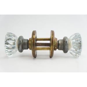 May include: Antique glass door knobs with a brass and metal connecting rod. The clear glass knobs have a ribbed design. The metal components show signs of age and wear, adding to the vintage aesthetic. A classic hardware piece.