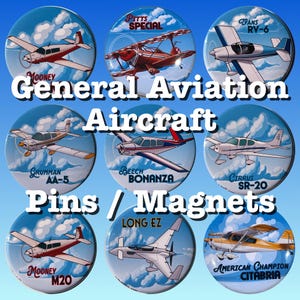 May include: A collection of round pins or magnets featuring various general aviation aircraft designs. Each pin displays a different airplane model, set against a blue sky background with clouds. Text includes aircraft names and model designations.