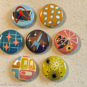 May include: Set of seven retro-style pinback buttons with various colorful designs, including a rocket ship, stars, and geometric patterns.