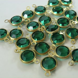 May include: A group of emerald green glass beads with gold-toned metal accents. Each bead has two loops for attaching to jewelry or other crafts.