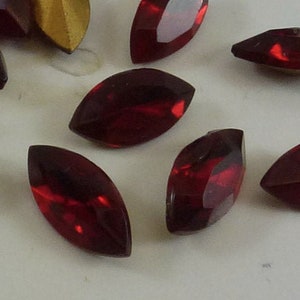 以下が含まれることがあります： 白い表面に散らばった、22個の赤いファセットカットのマルキーズ型のガラスラインストーンのセットです。