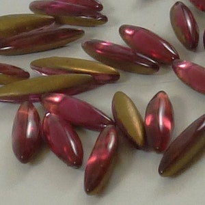 Può includere: Una collezione di circa 40 perline di vetro in due colori: oro e un rosa intenso. Le perline sono di forma ovale e hanno una finitura lucida.