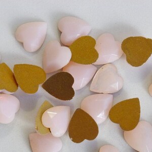 Può includere: Una collezione di strass a forma di cuore rosa, alcuni con retro dorato.