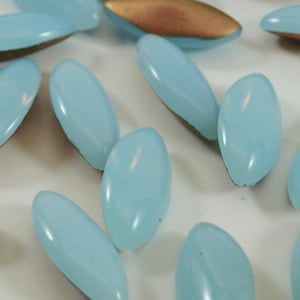 Peut inclure: Un ensemble de perles en verre bleu clair avec un dos doré. Les perles sont de forme ovale et ont une finition lisse et brillante.