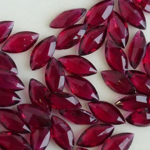 Peut inclure: Un groupe de pierres précieuses en verre de forme marquise facettées de couleur marron. Les pierres sont disposées de manière aléatoire sur une surface blanche.