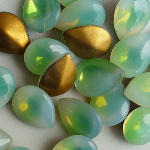 May include: A collection of iridescent green teardrop-shaped glass beads with a gold foil backing.
