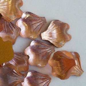 May include: A collection of approximately 20 copper-colored metal flower petals. The petals are all the same shape and size, and they have a slightly textured surface.