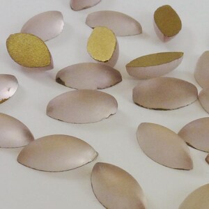 Peut inclure: Une collection de cabochons en verre ovales de couleur rose pâle. Certains cabochons ont un dos doré.