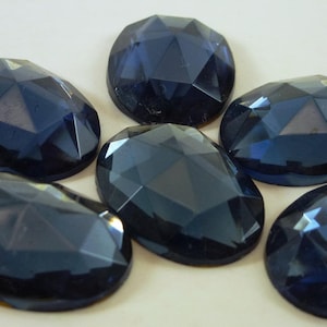 Op de afbeelding: Zes donkerblauwe ovale facetgeslepen glazen strasssteentjes.
