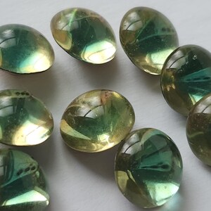May include: A selection of oval glass beads in green and yellow hues. The beads have a smooth, polished finish and reflect light, producing a shimmering effect. These decorative beads are suitable for jewellery making or craft projects.