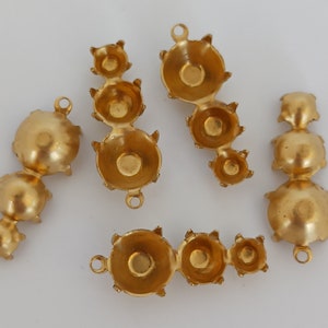 May include: Four gold-toned metal settings for attaching rhinestones or other embellishments. Each setting has three prongs and a loop for attaching to a jewelry piece.