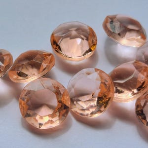 May include: A collection of round, faceted gemstones in a translucent peach-orange hue. Each stone features a brilliant cut with multiple triangular facets that reflect light, creating a sparkling appearance across the circular surfaces.