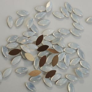 Può includere: Una grande quantità di strass bianchi a forma ovale. Gli strass sono sparsi su una superficie bianca.