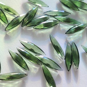 May include: A collection of green glass teardrop-shaped beads. The beads are faceted and have a translucent appearance.