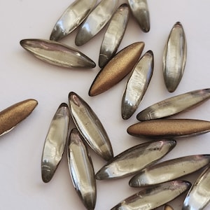 May include: A collection of glass beads in silver and gold tones. The beads are oval shaped and have a glossy finish.
