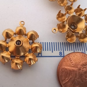 Op de afbeelding: Gouden metalen setting met acht pinnen om een ​​strasssteen of andere versiering te bevestigen. De setting heeft een klein gaatje in het midden om aan een sieraad te bevestigen.