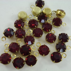 May include: A collection of red rhinestone embellishments with gold-toned metal settings and loops. The rhinestones are round and have a faceted design.