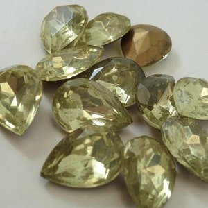 Puede incluir: Un grupo de 12 piedras de cristal de color verde claro en forma de lágrima. Las piedras tienen una superficie brillante y reflectante.