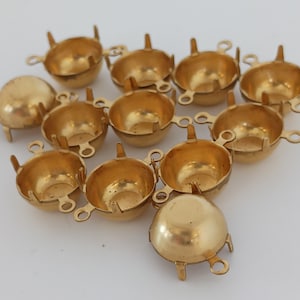 May include: A group of 12 gold-toned metal cup settings for jewellery making. Each setting has a round cup with three prongs on the bottom and two loops on the sides.