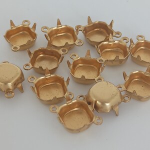 May include: A group of 12 gold-toned metal settings for cabochons. Each setting has four prongs and three loops. The settings are designed to hold a square or round stone.
