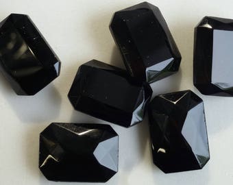 May include: Six black, faceted, rectangular glass gems. The gems are shiny and have a smooth surface.