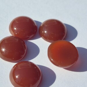 May include: Several polished, round, reddish-brown gemstones are displayed. The stones have a smooth, glossy surface and are set against a white backdrop. These gemstones are likely intended for jewellery making or craft projects.
