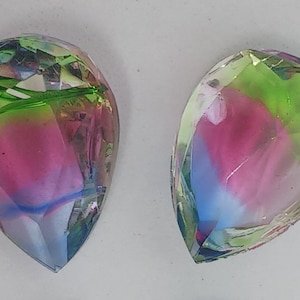 Puede incluir: Dos cuentas de vidrio en forma de lágrima con un acabado iridiscente multicolor. Las cuentas son una mezcla de rosa, verde, azul y blanco.