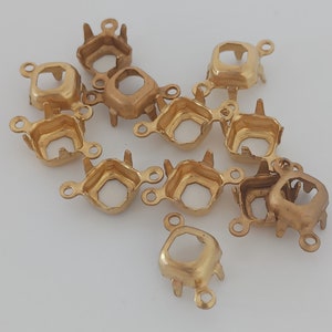 May include: A group of 12 gold-toned metal settings for square-shaped cabochons. Each setting has four prongs and two loops for attaching to jewelry.