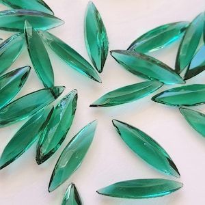 May include: A collection of emerald green glass teardrop-shaped beads. The beads are scattered on a white surface.