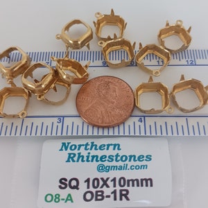 May include: Ten gold-toned metal settings for 10mm square rhinestones. The settings have a prong setting and a loop for attaching to a jewelry piece. The settings are shown next to a US penny for scale. The text on the label reads "Northern Rhinestones @gmail.com SQ 10X10mm 08-A OB-1R".