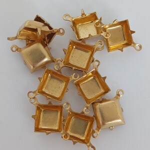 May include: A set of ten gold-toned metal settings for attaching rhinestones or other embellishments. Each setting has a square shape with four prongs and a loop for attaching to a project.