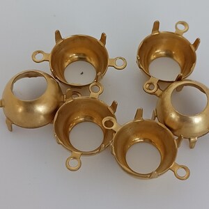 May include: Six gold-toned metal settings for cabochon stones. Each setting has a round opening and three prongs on the bottom.