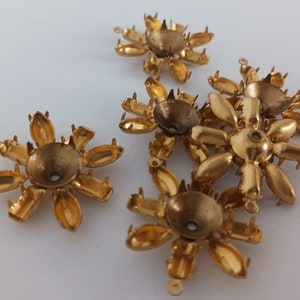 May include: Six gold-toned metal flower-shaped embellishments with prongs on the back. The embellishments are designed to be used for crafts and jewellery making.
