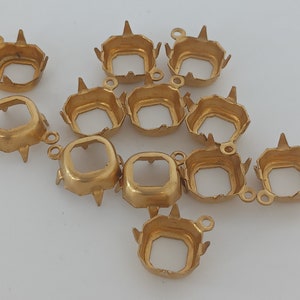 May include: A group of 12 gold-toned metal settings for square-shaped gemstones. The settings have a pronged edge and a loop for attaching to jewelry.