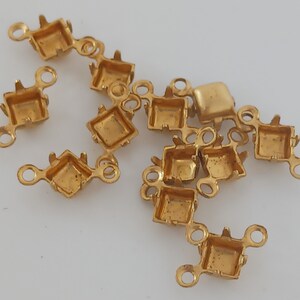 May include: A group of gold-toned metal settings for rhinestones or other embellishments. Each setting has a square shape with four prongs and two loops on the sides.