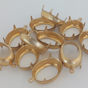 May include: A group of ten gold-toned metal oval-shaped bezel settings with prongs around the edges. The bezels have a loop on one side for attaching to a jewelry piece.