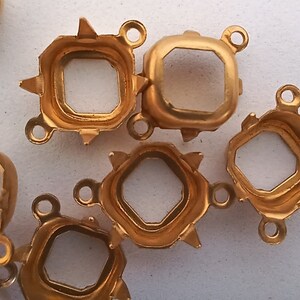 May include: Gold-toned metal settings for attaching gemstones or other jewelry components. Each setting has a square shape with a pointed edge and a loop on each side.