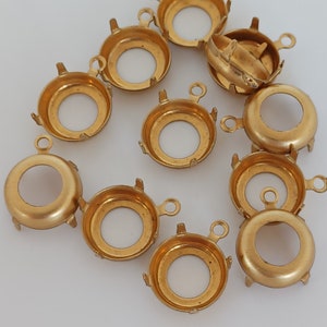 May include: A group of 10 gold-toned metal settings for cabochon stones. Each setting has four prongs and a loop for attaching to a piece of jewellery.