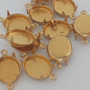 Könnte beinhalten: Eine Gruppe von ovalen, goldfarbenen Metallfassungen mit drei Zinken an der Unterseite und einer Öse an jeder Seite. Die Fassungen sind für das Einsetzen eines Cabochonsteins oder anderer Verzierungen gedacht.