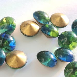 May include: A selection of decorative glass marbles and gold-coloured, cone-shaped objects. The marbles are a mix of green and blue, with a swirling pattern. The gold objects have a metallic finish.