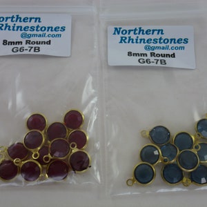 May include: Two bags of 8mm round rhinestones with gold jump rings. One bag contains burgundy rhinestones and the other contains blue rhinestones. The bags are labeled "Northern Rhinestones @gmail.com 8mm Round G6-7B".