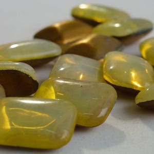 Könnte beinhalten: Eine Sammlung gelber Glasfliesen mit leicht schimmerndem Finish. Die Fliesen sind glatt und haben eine leicht abgerundete Form.