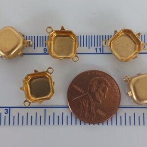 Może przedstawiać: Pięć złotych metalowych opraw do kaboszon&oacute;w, każda z trzema szponami i dwoma pętlami. Oprawy mają średnicę około 2,5 cm i są pokazane obok amerykańskiego centa dla skali.