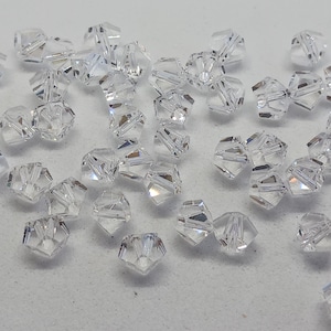 May include: A collection of clear glass beads with a faceted design. The beads are scattered on a white surface.