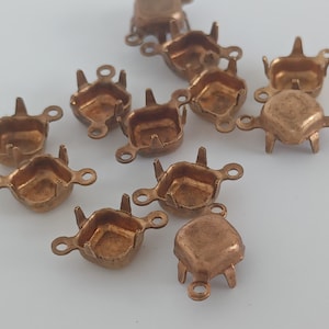 May include: A group of 10 copper-colored metal settings for attaching rhinestones or other embellishments. Each setting has four prongs and a square-shaped opening.
