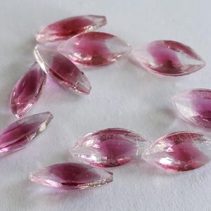 Puede incluir: Una colección de cuentas de vidrio en forma de lágrima de color rosa y transparente. Las cuentas son iridiscentes y tienen un brillo sutil.