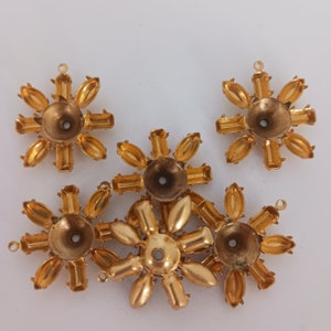 May include: Six gold-toned metal flower-shaped embellishments with a hole in the center. Each embellishment has eight points and a slightly raised center.